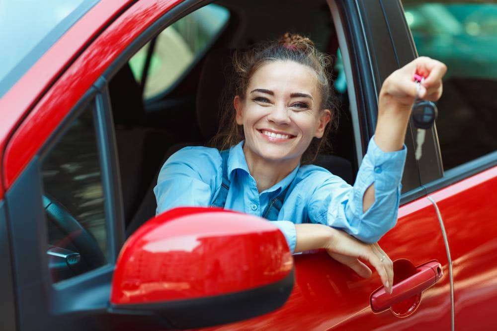Young woman showing keys of a red rental car